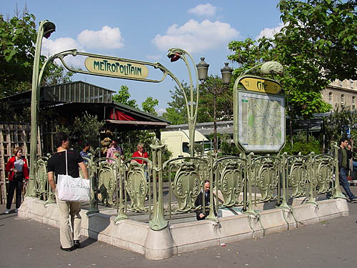 Staircase descending from sidewalk is labelled METROPOLITAIN in a typeface with varying capital heights. The entrance is surrounded by green wrought-iron shields