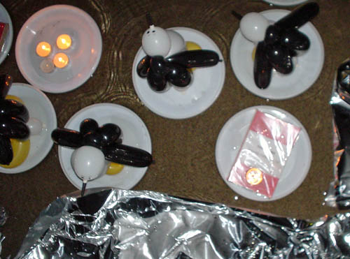 Paper plates holding model penguins made out of black, white, and yellow balloons float alongside other plates carrying a plastic-wrapped book and votive candles