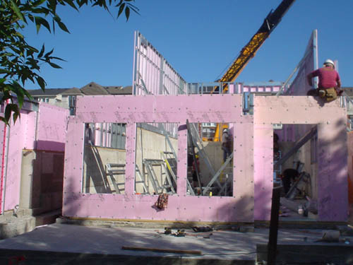 Workman sits on top edge of pink-insulation-covered wall at construction site