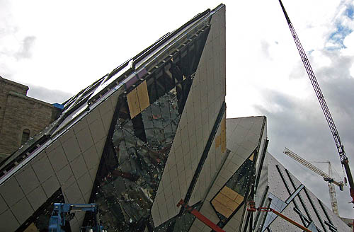 White angular forms, one of which has a strip half-covered in glass, project like mountains from a stone building