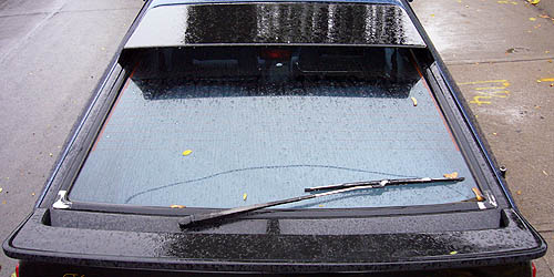 Raindrops and leaves cover the upper and lower spoilers, backlight, and rear wiper of a black car