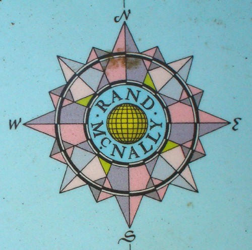 Compass set against sea-blue background reads RAND McNALLY at centre, has jewelled and faceted arms, and uses script capitals for N, E, S, W