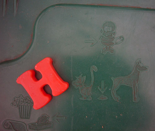 Orange Cooper Black fridge-magnet H on green plastic object embossed with pictographs