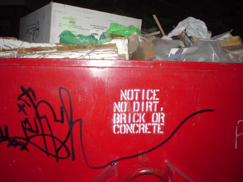 Red dumpster graffitied with ‘Notice: No dirt, brick or concrete’