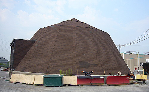 Large cone-like structure,  made of tarpaper and with a large doorway on the left side, sits on a concrete pad