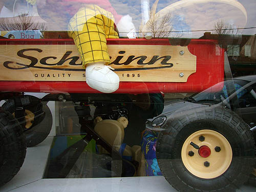 Rag-doll arm hangs over the side of a red Schwinn children’s wagon in a shop window
