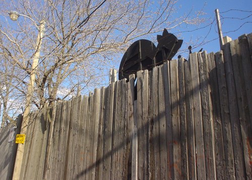 Backside of wooden cat atop haggard wooden fence