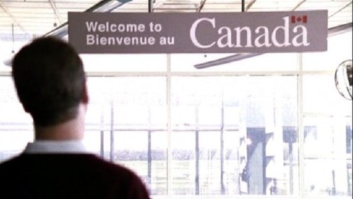 Coupland facing a hanging sign reading Welcome to Bienvenue au Canada