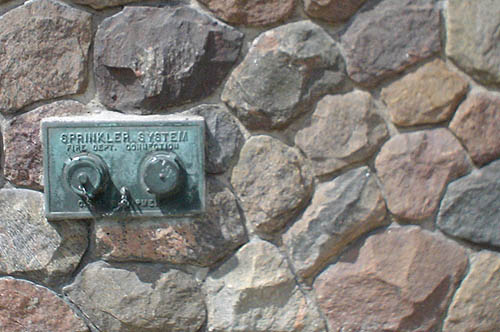 Two-pipe panel labelled SPRINKLER SYSTEM is installed in a stone wall
