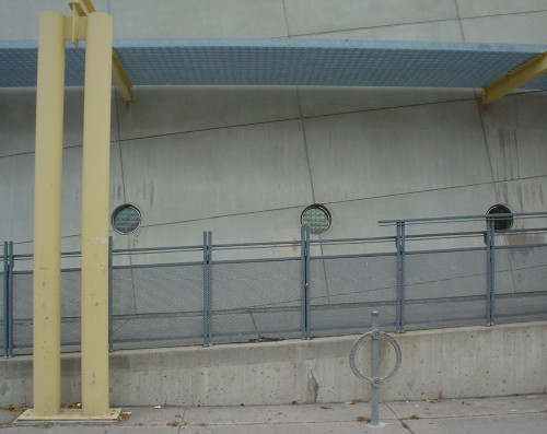 Concrete wall behind grey wheelchair ramp shows three porthole windows