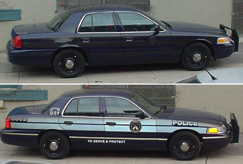 Ford Crown Victoria police cruiser. Flash photo ‘illuminates’ decals showing car number [6002], police insignia, telephone icon and ‘9-1-1,’ ‘To Serve and Protect’ slogan, and body-side stripes. In daylight photo, no markings are visible save for vestigial insignia