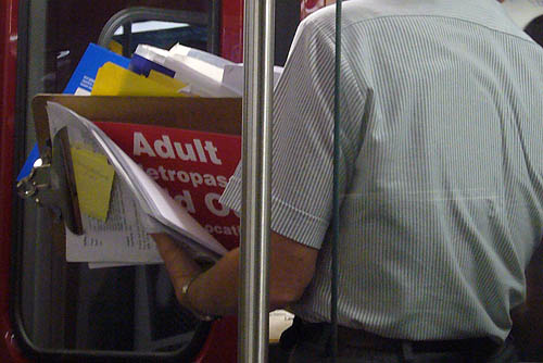 Person in striped shirt, seen from neck to waist, holds clipboard with a visible sign amid the papers: Adult etropass