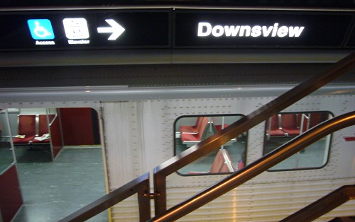 Sign over parked subway car has blurry pictographs and less-legible word Downsview