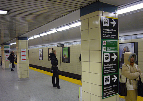 Subway station with three pillars, one of which has preprinted signs and two of which have laser-printed signs with red arrows
