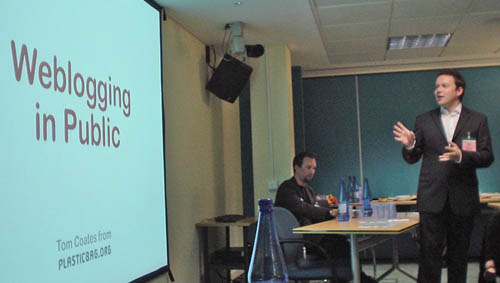 Tom Coates, in suit and shirt, gestures to screen bearing the words ‘Weblogging in Public’ in Arial Roudned