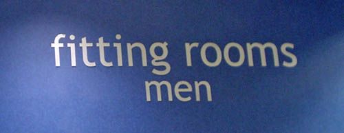 Sign reads ‘fitting rooms men’ in Trebuchet