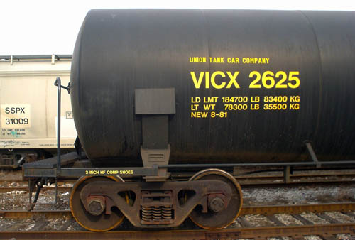Black railcar with dirty streaks sits on rusted wheels and rusted track and is labeled VICX 2625 (with other weight measurements) in yellow Helvetica