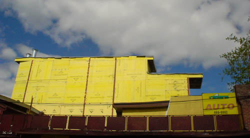 Two-storey extension of building has the shape of a locomotive and is finished in bright-yellow Tyvek against a cloudy blue sky