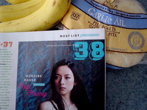 A bag of garlic pitas, bananas, and a corner of a magazine page showing a photo of Ziyi Zhang, with a script font whose crossed Zs are hard to discern