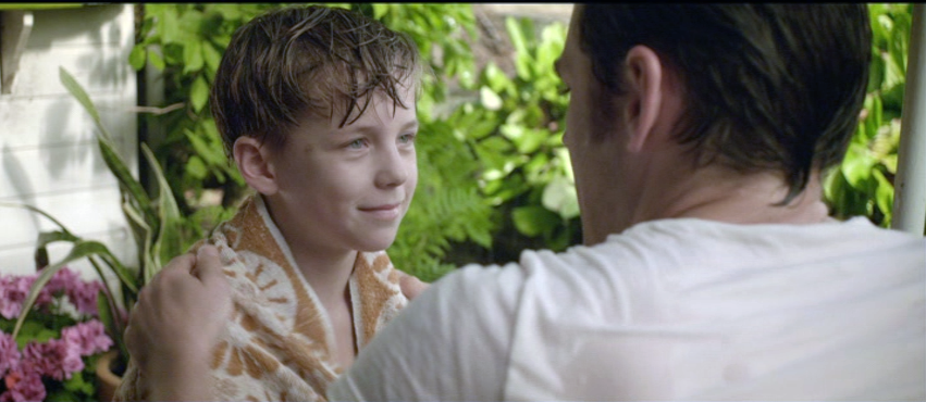 Workman dries off a young lad with a towel as the lad smiles and gazes at him