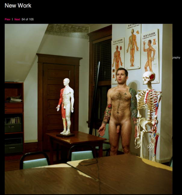 Naked man with tattooed left arm stands in study alongside skeletal and full-body medical models and illustrations