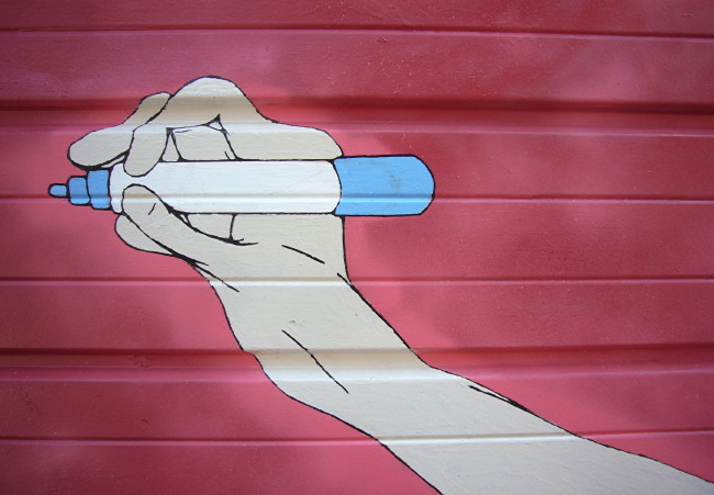 Graffiti on red wall shows a hand holding a blue marker perfectly horizontal