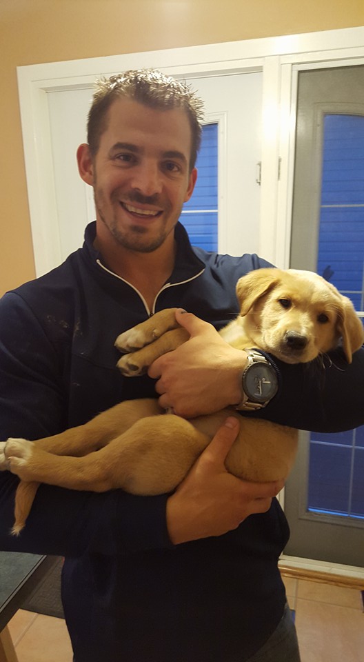 Handsome young man smiles while cradling an unhappy-looking puppy