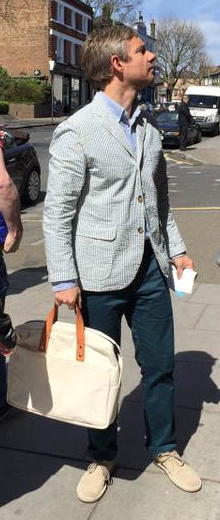 Martin Freeman in pale-blue streiped blazer, blue shirt, indigo pantalon, and bright beige nubuck shoes, with bone-colouted canvas bag with tan leather straps