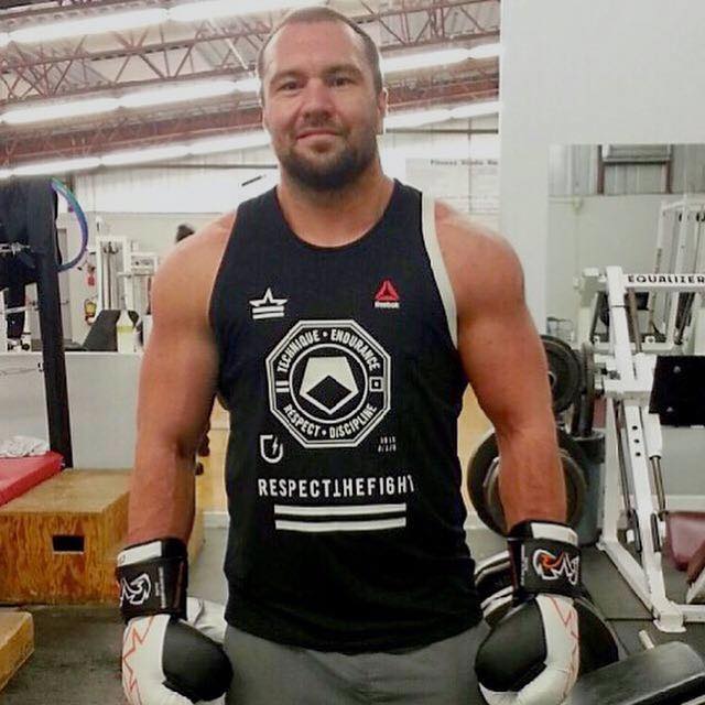 Muscular man in cutoff T-shirt and boxing gloves standing in weight room