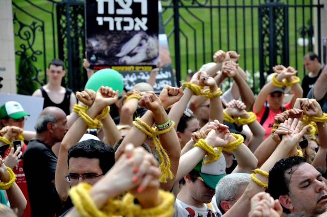 Protesters raise their hands over their heads, crossed wrists bound with yellow rope