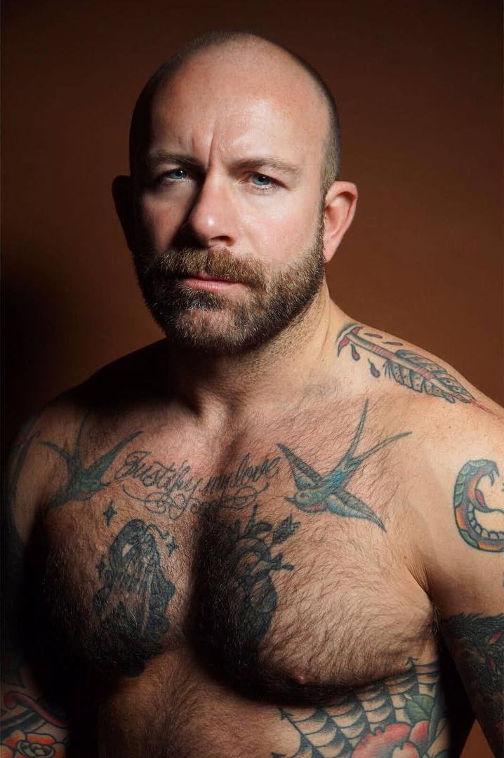 Severely tattooed muscular baldie against bronze background