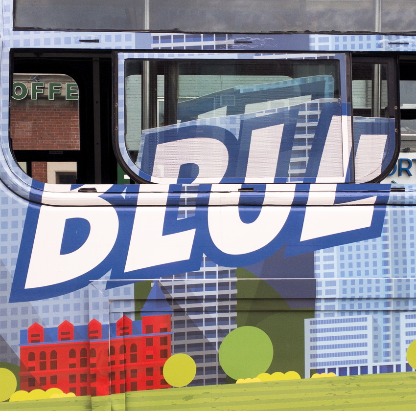 Large letters, printed on vinyl wrap across sidewall and opened windows of streetcar, read BLUE or BRUL