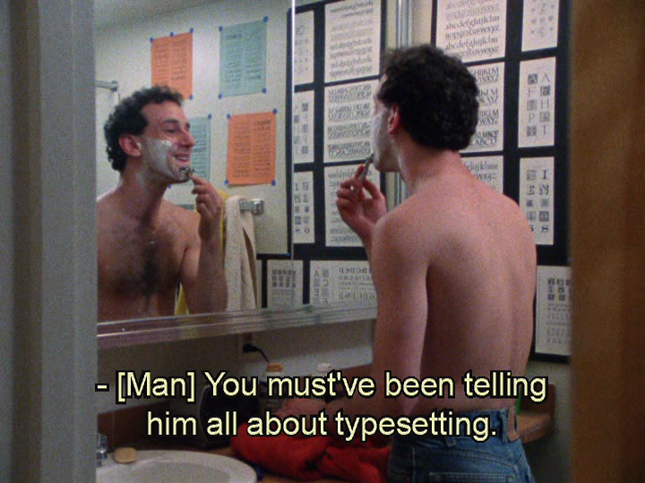 Man shaving at mirror with typeface posters on wall