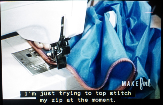 Blue anorak with red zipper in sewing machine. “I’m just trying to top-stitch my zip at the moment”