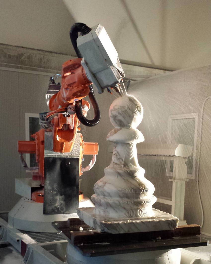 Lathe attachment on lobster-coloured industrial robot drills the spherical tip of a huge marble pawn