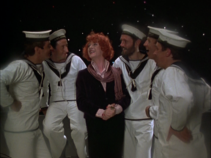 Mr. Crisp, in red-hennaed hair and a scarf, beams brightly as five sailors surround him good-naturedly