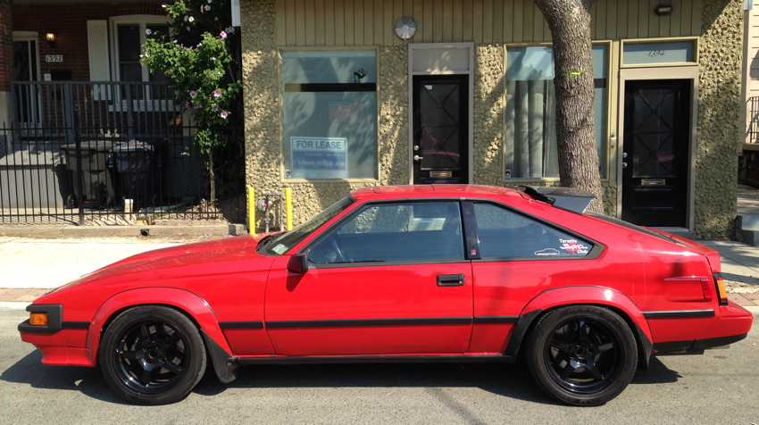 Red Supra hatchback, with flared feners, textured hood, smoked-glass high-mounted spiler, flanges around side marker lights