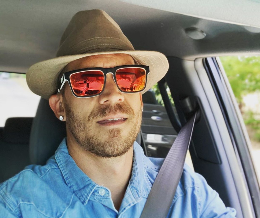 Russell Harvard, in mirrored yellow shades and a hat, behind the wheel