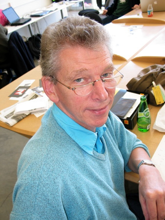 Bemused-looking man in blue sweater, glasses low on nose, regards us over his shoulder