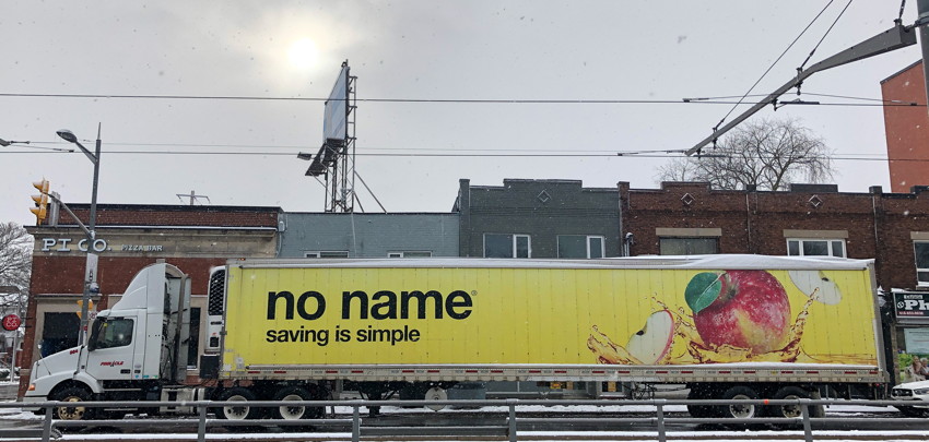 Giant trailer on 18-wheeler at wintry intersection is yellow with slogan: no name® saving is simple